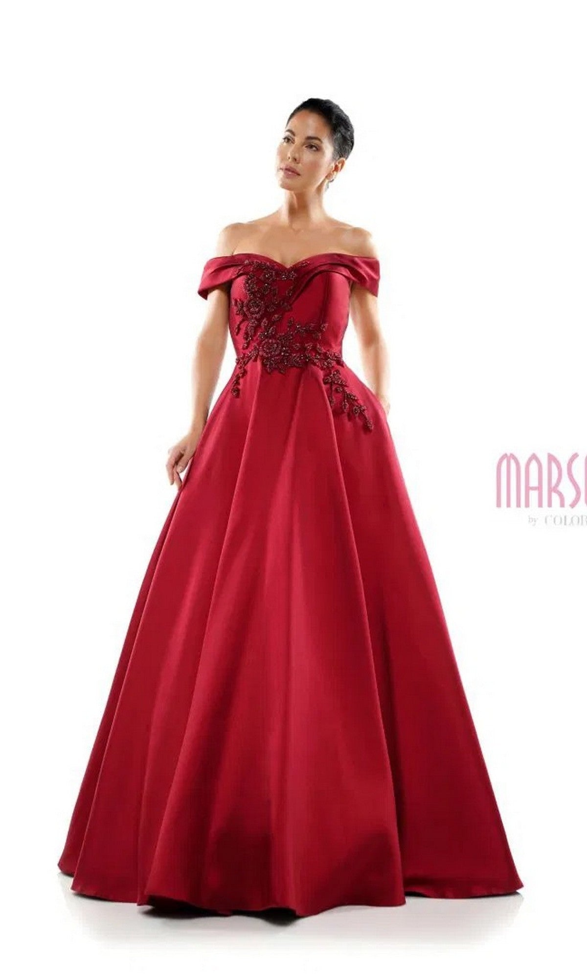 A woman stands against a plain white background wearing the Marsoni MV1008 Long Formal Dress in wine, an off-the-shoulder floor-length gown featuring floral embroidery and delicate beaded appliqué on the bodice.